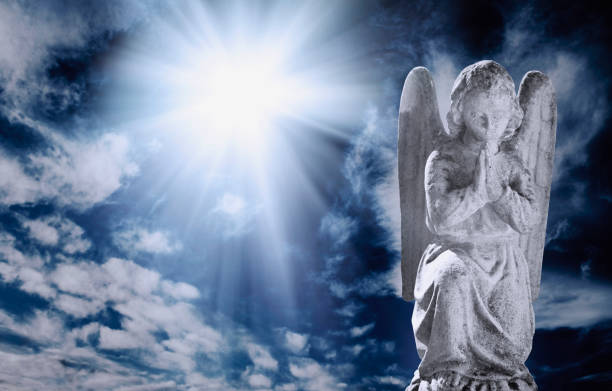 Ancient statueof angel in rays of light against sky with clouds