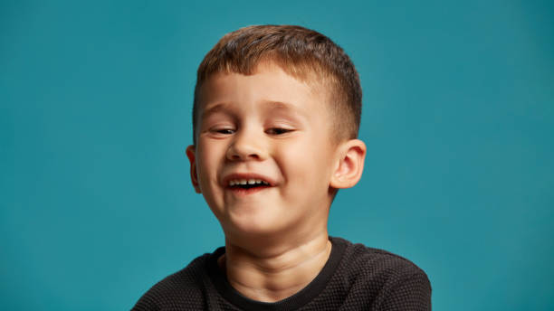 istock Boy lets out soft chuckle, satisfied and light-hearted expression on his face against blue studio background. Have fun. Funny jokes. 2183458789
