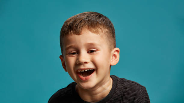 istock Boy laughing, with satisfied and light-hearted expression on his face against blue studio background. Have fun. Funny jokes. 2183458790