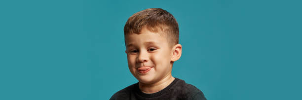 istock Sticking his tongue out, boy shows off his playful side against blue studio background. His expression full of character and youthful charm. 2183458794