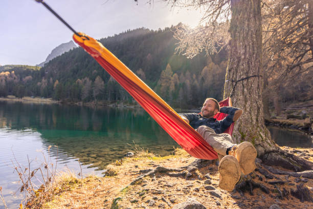 istock Man Relaxing in Hammock by Lake with Autumn Forest View 2183459629