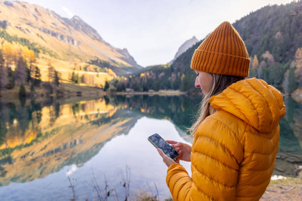 istock Woman Scrolling Through Phone by Reflective Mountain Lake in Autumn 2183459880