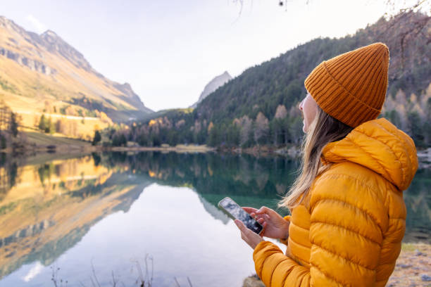 istock Woman Scrolling Through Phone by Reflective Mountain Lake in Autumn 2183459885