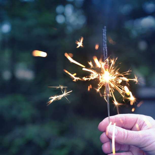 istock hand holding sparkler on fir trees on Christmas evening 2183461375