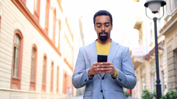 istock Black man texting on his phone as he walks through a city sidewalk 2183481703