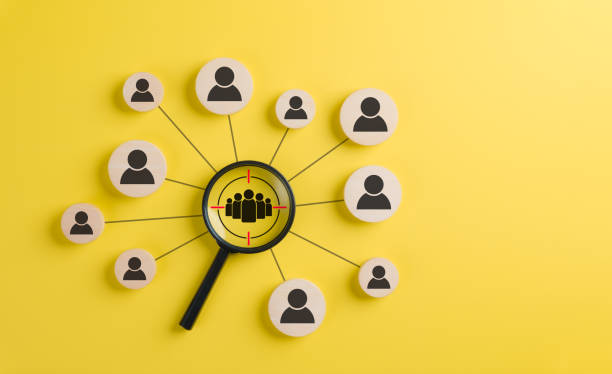 istock Target audience and customer focus concept. A black magnifying glass highlighting a group of people icons on wooden circles, representing audience targeting, customer focus, digital marketing strategy 2183482555
