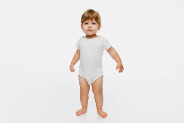 istock Curious baby standing with arms slightly raised, against white studio background, capturing innocence and wonder of early childhood. 2183482652