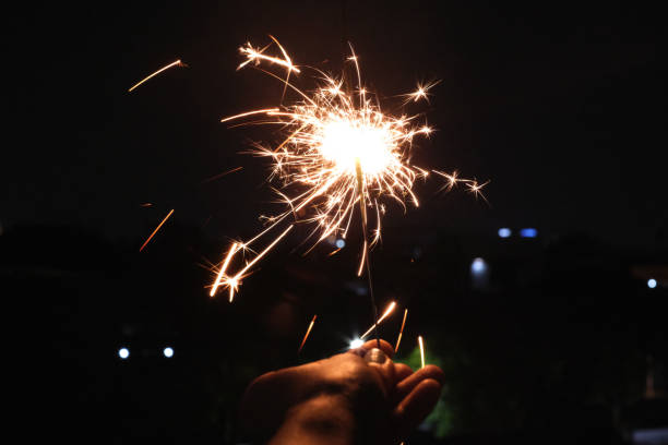 Shot of unrecognizable hand Playing Sparklers on New Year Eve, in the dark. Concept: Solo Sparkler Celebration: Embracing the New Year in Solitude, sparkler light, personal celebration, festive glow, reflective moments, quiet joy, holiday tradition, nighttime ambiance, sparkling light