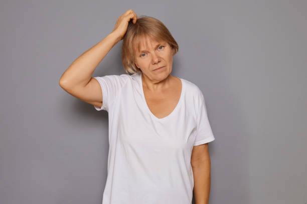 istock Senior woman thinking thoughtfully rubbing her head and grimacing pondering solution to query being in deep contemplation isolated over gray background 2183489321