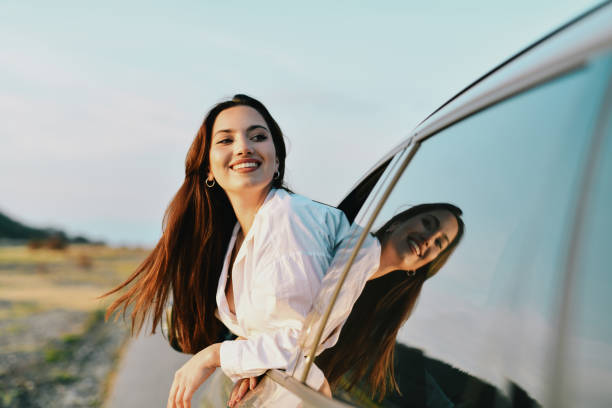 istock Gorgeous Female With Beautiful Smile Leaning on Car Window Enjoying Sunset 2183493507