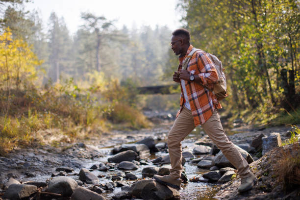 istock Smiling man crossing river while hiking in the forest 2183498902