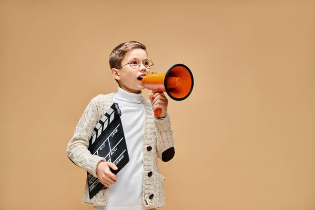 istock Charming little boy in cozy sweater enthusiastically directing with a megaphone and clapperboard 2183499362