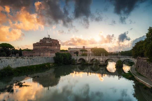 Rome, Italy - September 10, 2022: Fiery clouds at sunrise above medieval St. Angelo castle and the bridge over Tiber river in Rome, Italy