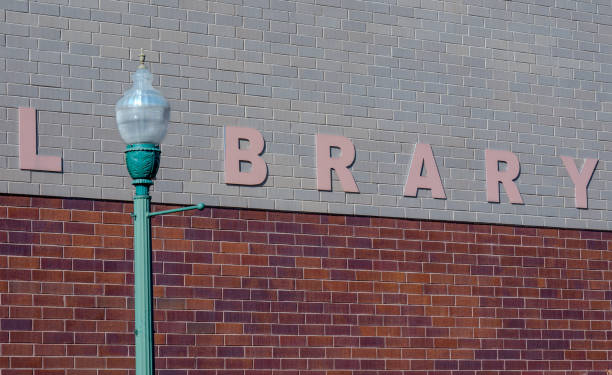 A classic green street lamp stands in front of a brick wall with visible large letters, showcasing an urban architectural element.