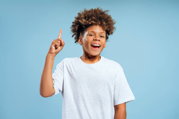 istock Smiling authentic African American boy with curly hair looking at camera pointing finger having idea 2183503898