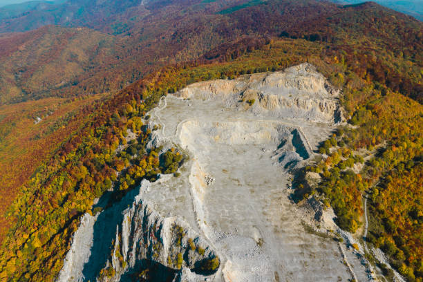 Aerial view of a rugged limestone quarry with exposed rocky terrain and distinct geological formations under a clear blue sky. The barren land and rough stone textures highlight the area's mining activity and natural erosion.