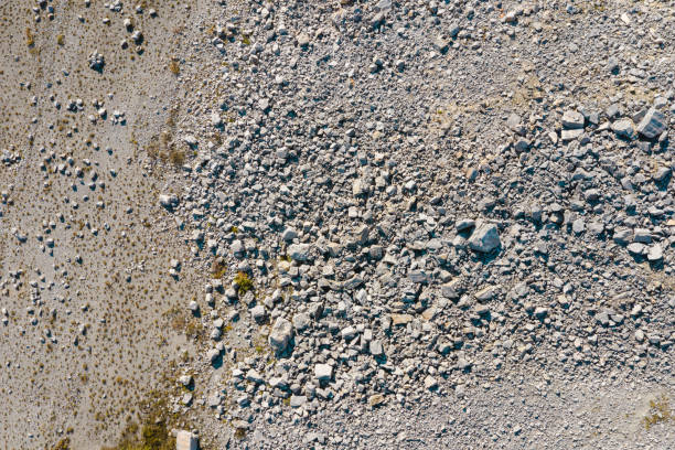 Aerial top-down view of a barren, rocky landscape with sparse patches of vegetation scattered across the surface. The minimal plant growth and scattered rocks highlight the arid and rugged nature of the terrain.