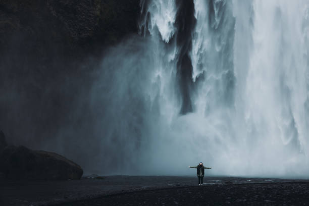 Silhouette of female tourist  raising arms and feeling happiness to explore breathtaking Skogafoss waterfall walking with dramatic Nordic views in South Iceland