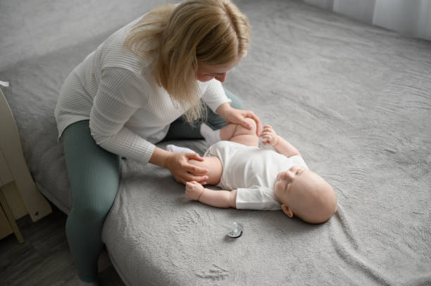 Baby lies on bed at home, mom does morning exercises for infant, bending and unbending legs, legs to stomach, strengthening muscles, preventing baby gases, fighting muscle hypertonicity in newborn el bebé se acuesta en la cama en casa, mamá hace ejercicios matutinos para el bebé, doblando y flexionando las piernas, las piernas al estómago, fortaleciendo los músculos, previniendo los gases del bebé, combatiendo la hipertonicidad muscular en el