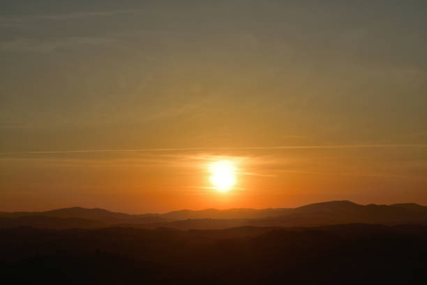 The orange sunset and its rays dazzle the green forests and meadows