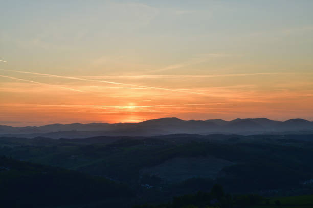 The orange sunset and its rays dazzle the green forests and meadows