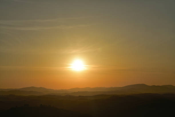 The orange sunset and its rays dazzle the green forests and meadows