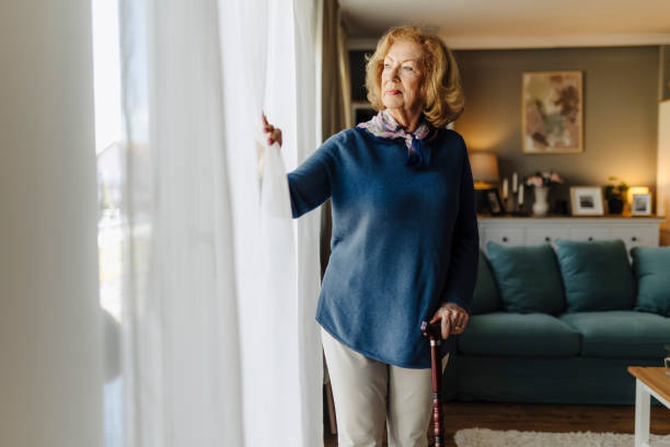 istock Senior woman standing by a window with a cane 2183525605
