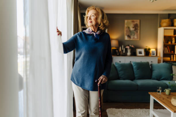 istock Senior woman standing by a window with a cane 2183526373