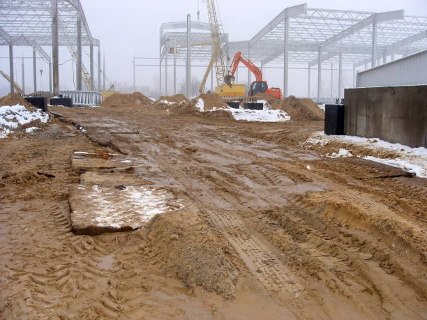 istock Construction site with steel framework and muddy ground, machinery in the background. 2183528213