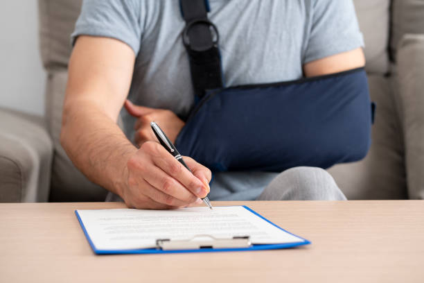 handicapped man with sling signing contract at home Front view of a handicapped man with sling signing contract at home man with arm sling stock pictures, royalty-free photos & images