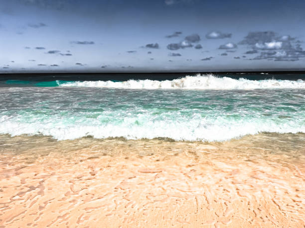 sandy beach with waves crashing through turquoise water with gray sky