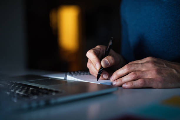 istock Close up of man working from home office at evening, writing notes in planner. Telecommuting and home office. 2183533316