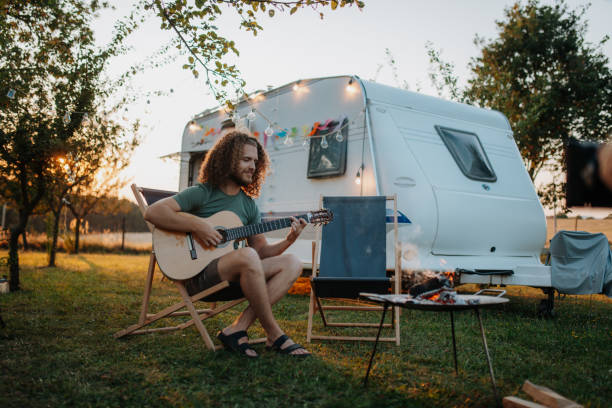 istock Young man is on a camping trip in nature alone, sitting in front caravan and playing guitar. 2183534327