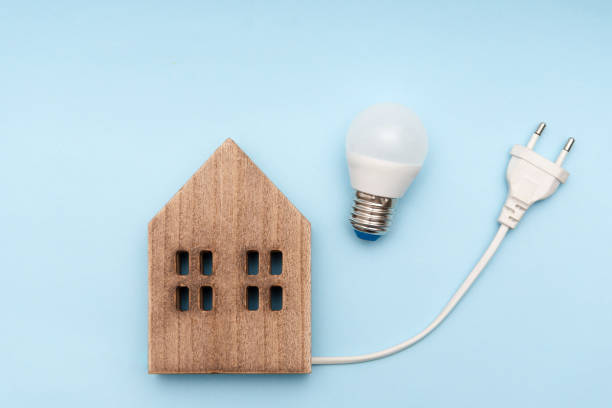 istock Energy Efficient Home Concept, Wooden House Model with LED Light Bulb and Electrical Plug on Blue Background 2183538572