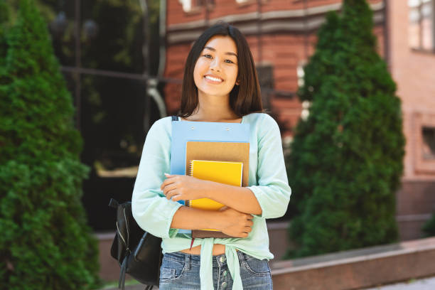 istock Smiling asian student girl with backpack and workbooks over college background 2183552920