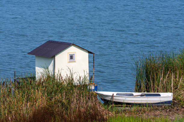 A small fishing house on a raft with a boat next to the shore on a lake.