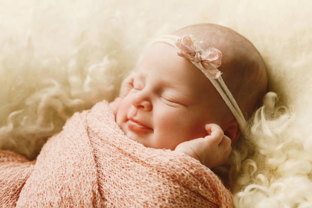 A newborn baby girl, eight days new, sleeps on a soft bed of wool.