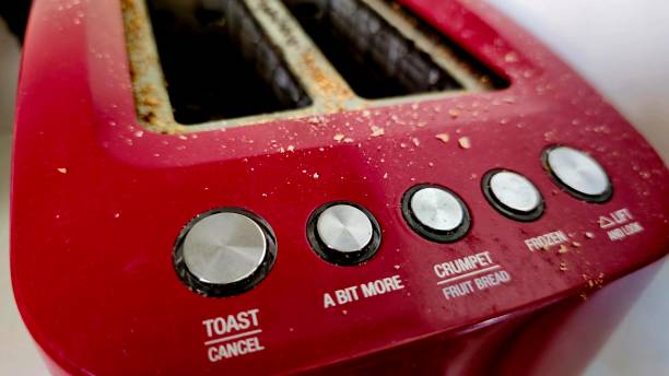 istock A red toaster with five buttons labeled 'toast cancel', 'a bit more', 'crumpet fruit bread', 'frozen', and 'life and look'. The toaster has visible crumbs and appears to be used. 2183602443