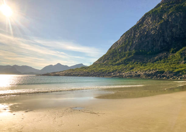 A summer evening on a small, secluded beach with calm waves, blue skies, and  green mountains in Henningsvaer, Norway