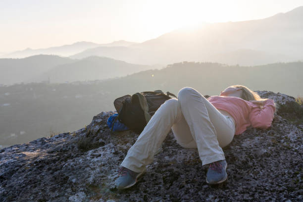 Young woman reclines on mountain top at sunset, distant hills, Liguria