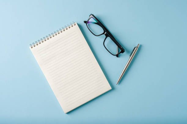 istock Top view of notebook, glasses and ballpoint pen on blue background 2183619338