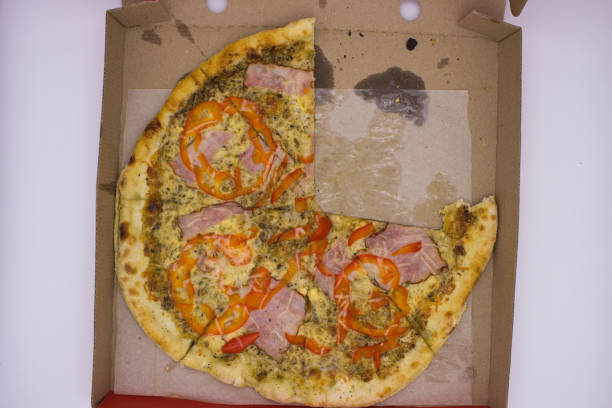 A view of a partially eaten pizza with slices of ham and red peppers in an open cardboard box. The remaining crust and oily marks give a sense of a shared meal experience.