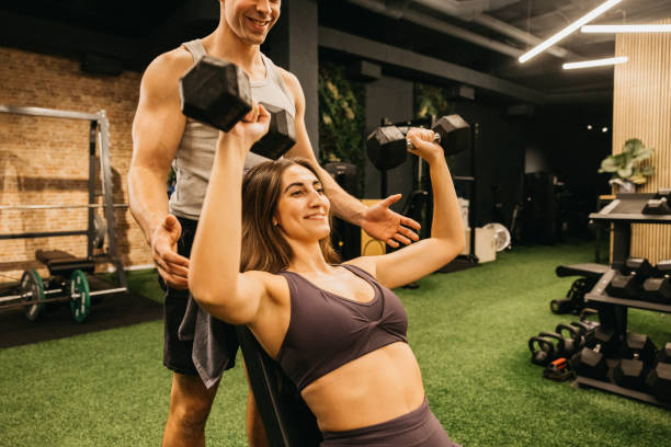 istock Woman lifting dumbbells with trainer assistance in a modern gym setting 2183626145