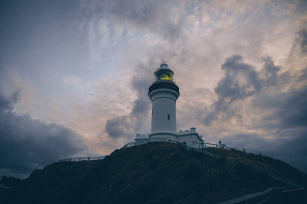 Witness the dramatic beauty of Cape Byron Lighthouse at sunset, perched on cliffs at Byron Bay, Australia, offering stunning views and a picturesque coastal landscape.
