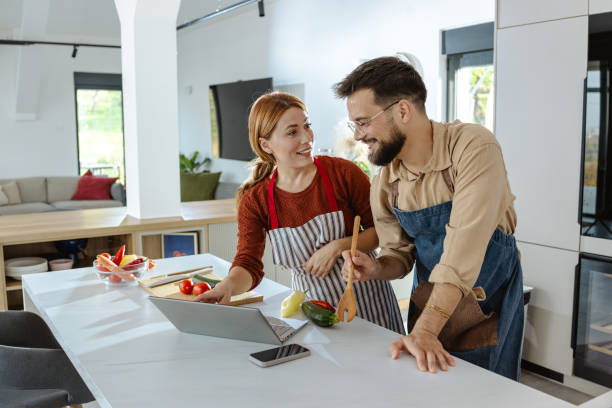istock Couple cooking together in modern kitchen using laptop for recipes 2183632112