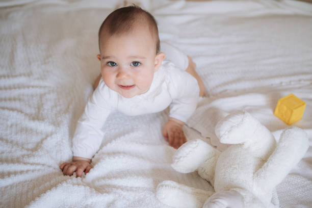 istock Smiling Baby Crawling on Bed with Soft Plush Toy 2183632368