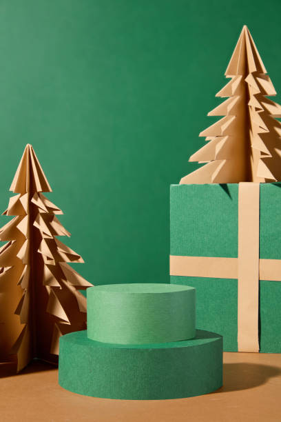 istock Christmas themed image template using an emerald background, a close-up of two stacked cylinders creating product display space, next to green gift boxes and two paper pine trees. 2183633412