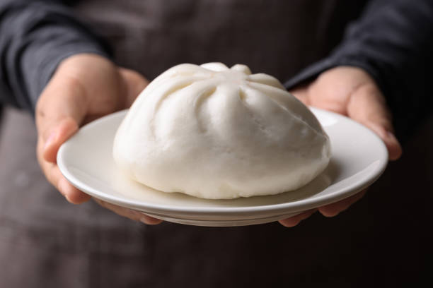 Asian steamed bun stuffed with pork and egg on plate holding by hand