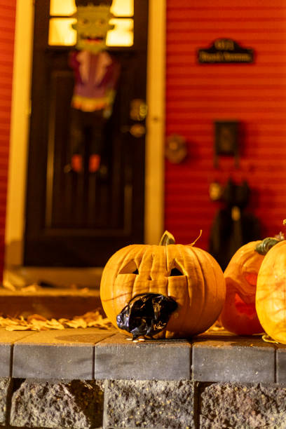 Pumpkins with carved grimaces, one of which is filled with black material, are placed on a brick platform in front of the front door