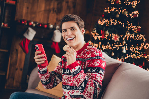 istock Photo of funky cool guy dressed ornament pullover enjoying x-mas day eating biscuits typing modern gadget indoors house apartment room 2183646387